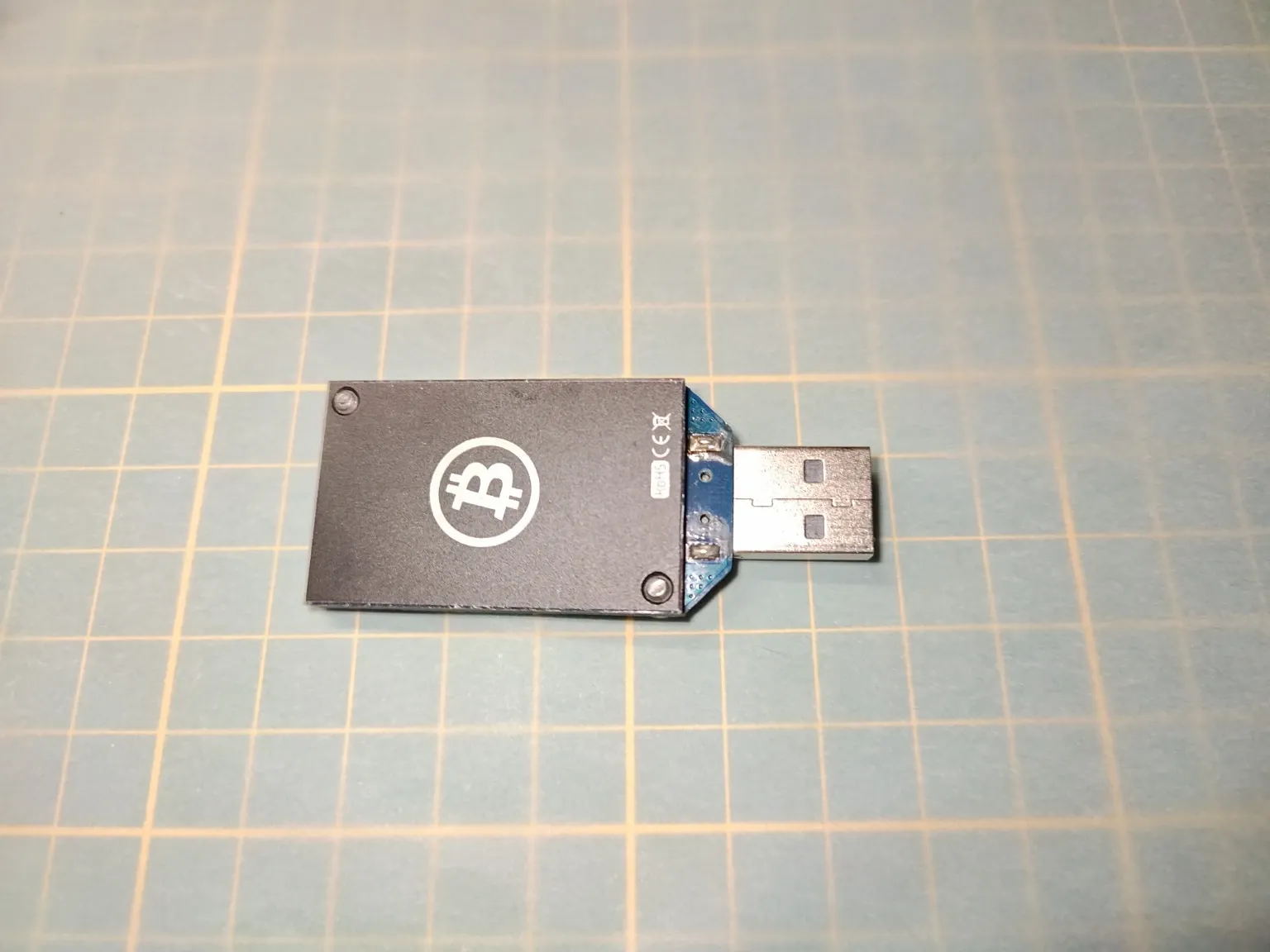 Historický USB Bitcoin ASICMiner Block Erupter Sapphire s původním černým chladičem a logem Bitcoinu.