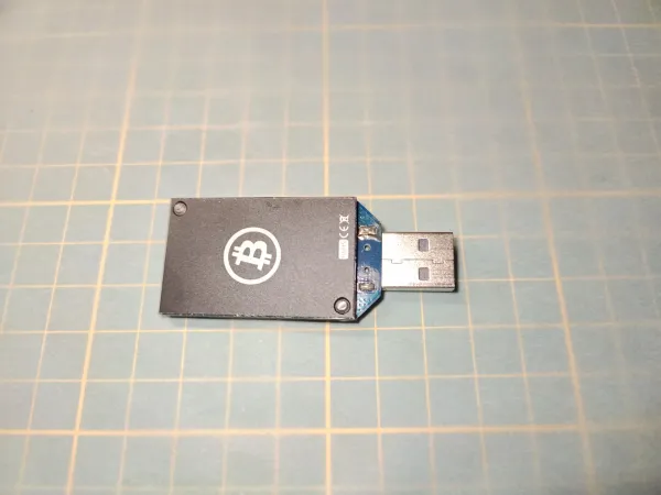 Historický USB Bitcoin ASICMiner Block Erupter Sapphire s původním černým chladičem a logem Bitcoinu.